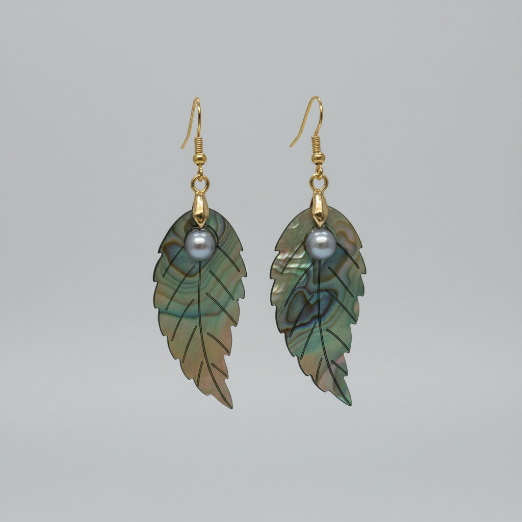 A pair of dangling leaf-shaped earrings with iridescent green and silver abalone shell leaves, a small gray pearl-like bead, and gold-tone hooks, displayed on a brown floral backing card.